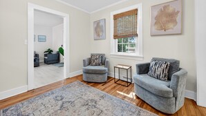 A living room with a gray sofa, a gray armchair, a small side table, and a large window with blinds. - Charming Coastal Retreat with Live Oaks (Georgetown)