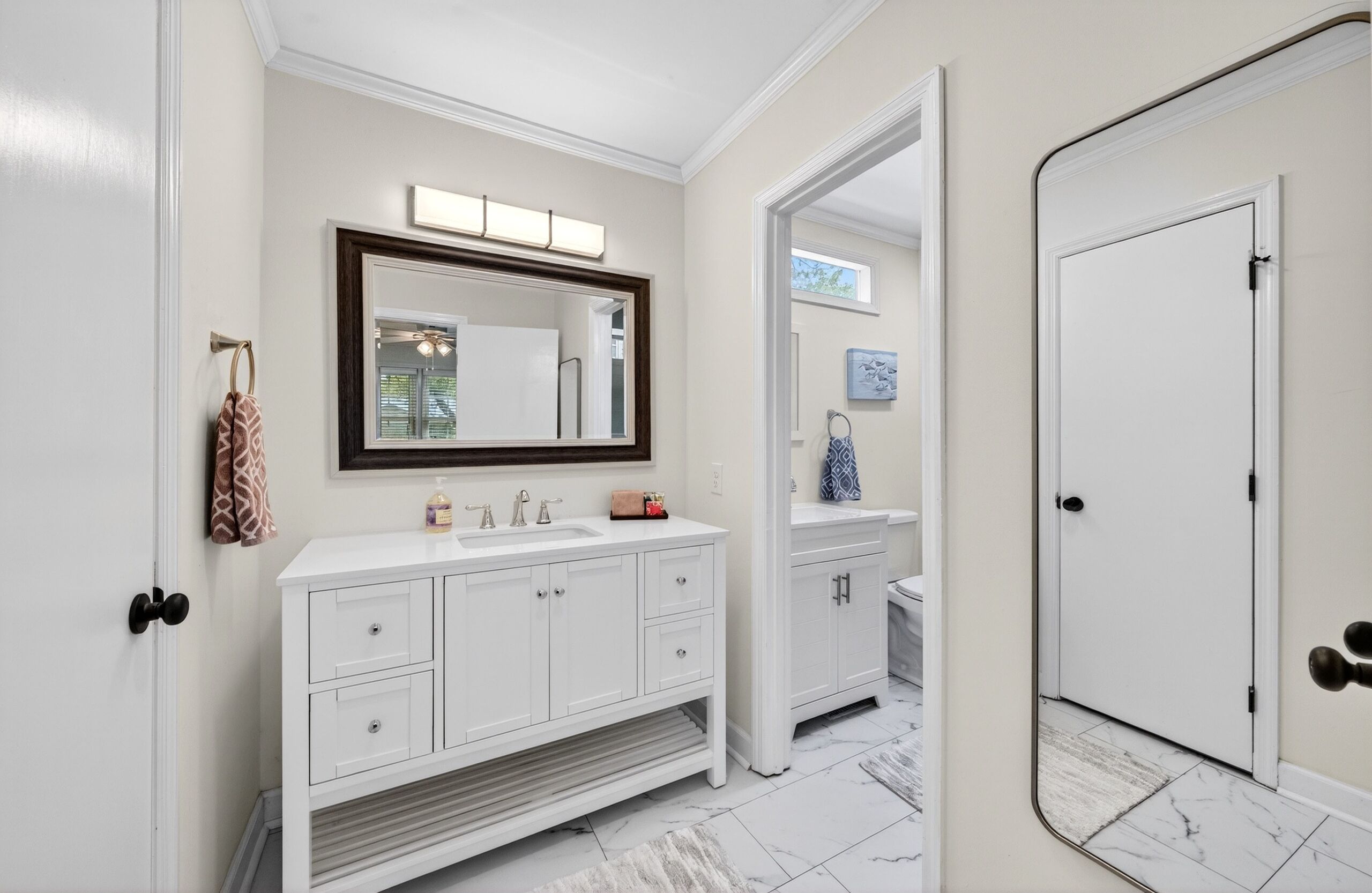 A bathroom with a white vanity, a large mirror, and a door leading to another room.