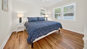 A bedroom with a bed, two bedside tables, a ceiling fan, and a window with blinds. - Charming Coastal Retreat with Live Oaks (Georgetown)