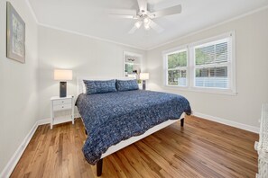 Ein Schlafzimmer mit einem Bett, zwei Nachttischen, einem Deckenventilator und einem Fenster mit Jalousien.