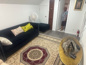 Ein Wohnzimmer mit schwarzem Sofa, einem gemusterten Teppich und einem kleinen runden Tisch mit dekorativer Basis.