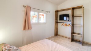 Ein Schlafzimmer mit einem Bett, einem an einer Holzwand montierten Fernseher, einem Fenster mit Vorhängen und einem Holzschrank.