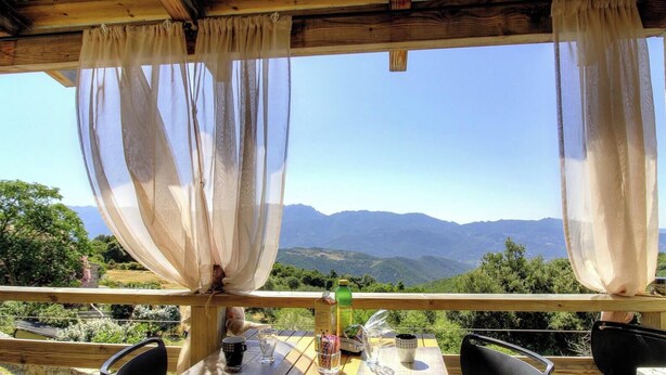 Eine Holzterrasse mit Tisch und Stühlen mit Blick auf eine gebirgige Landschaft.