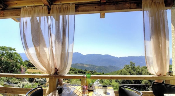 Eine Holzterrasse mit Tisch und Stühlen mit Blick auf eine gebirgige Landschaft.
