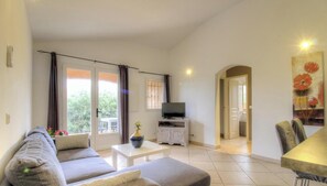 A living room with a sofa, TV, and a dining area with chairs. - Villa Léa - SAINTE LUCIE DE PORTO VECCHIO (SAINTE LUCIE DE PORTO VECCHIO)