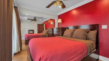 A bedroom with two beds, red walls, wooden headboards, and ceiling fans.
