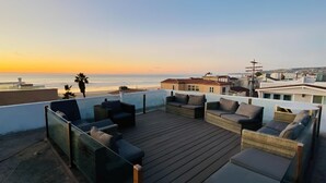 Eine Dachterrasse mit Sitzgelegenheiten im Freien und Blick auf den Ozean bei Sonnenuntergang.