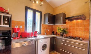 A kitchen with a washing machine, a coffee maker, and a stove. - The potter's cottage - PALNECA (PALNECA)