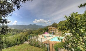 Ein Poolbereich mit Liegestühlen, ein kleines Gebäude und eine gebirgige Landschaft im Hintergrund.
