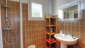 Kylpyhuone, jossa on suihku, pesuallas, peili ja hylly, jossa on hygieniatuotteita.