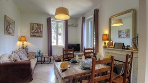 A living room with a sofa, dining table, chairs, a TV, and artwork on the walls. - Villa Charlain - PIETROSELLA (PIETROSELLA)