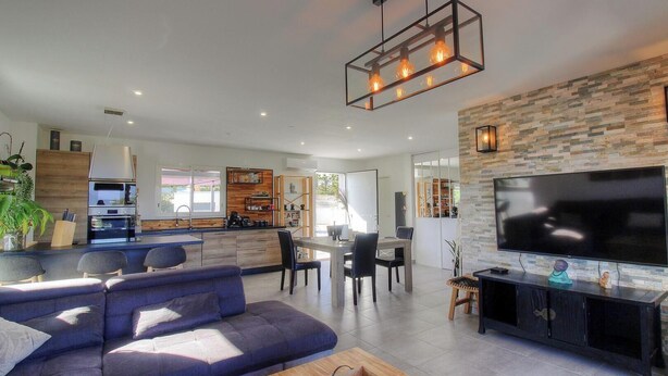 A modern kitchen with a built-in oven, a dining area with a table and chairs, a living room with a sofa and a TV, and a stone accent wall. - Le Spurtone - ALATA - Gîte (ALATA)