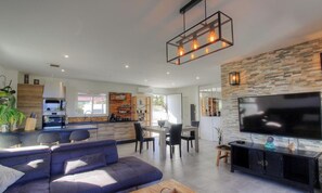 A modern kitchen with a built-in oven, a dining area with a table and chairs, a living room with a sofa and a TV, and a stone accent wall. - Le Spurtone - ALATA - Gîte (ALATA)