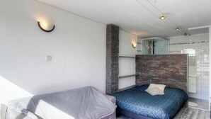 A modern bedroom with a bed, a chair, a brick accent wall, and a glass door leading to a bathroom. - Le Spurtone - ALATA - Gîte (ALATA)