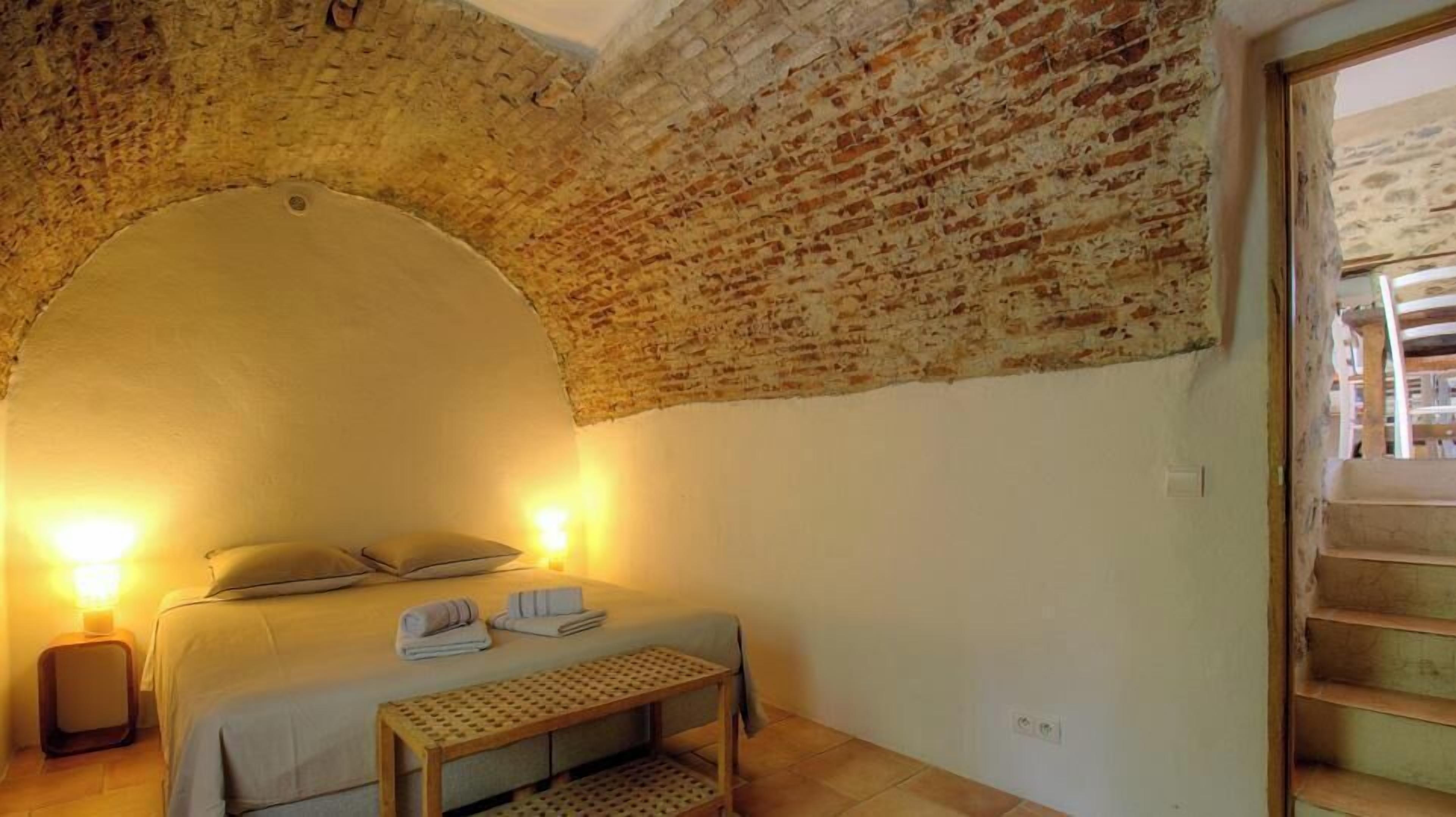 Une pièce comprenant un lit, une table de chevet, une lampe et une arche en briques.