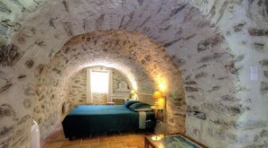 Ein Zimmer mit einer Decke aus Stein, einem Bett mit grüner Bettdecke, einem Nachttisch mit Lampe und einem Fenster mit Vorhängen.