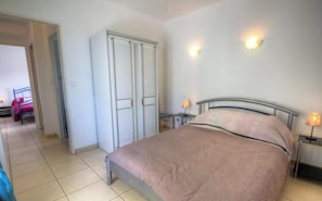 Ein Schlafzimmer mit Bett, Nachttischen, einem Kleiderschrank und einer Tür zu einem anderen Raum.