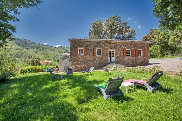 Un bâtiment en pierre avec une porte rouge, un escalier et un espace extérieur aménagé avec des tables et des parasols.