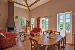 Ein Wohnzimmer mit Kamin, roten Möbeln, einem Esstisch mit Stühlen und großen Fenstern mit Ausblick.