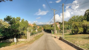 Camí rural vora vegetació i parets de pedra, amb pals de serveis i un cel clar.
