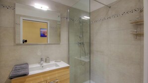 Ein modernes Badezimmer mit einer gläsernen Duschkabine, einem Waschbecken mit Spiegel darüber und einem Handtuch auf der Ablagefläche.