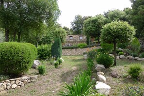 Ein Steinhaus mit einem Garten, der verschiedene Sträucher, Bäume und eine Steinmauer zeigt.