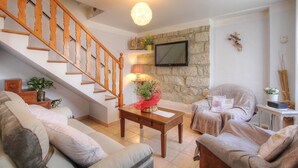 A living room with a wooden staircase, a stone wall, a flat-screen TV, and a cozy seating area. - A MOLINA - ZICAVO - Gîte (ZICAVO)