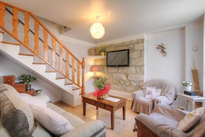 A living room with a wooden staircase, a stone wall, a flat-screen TV, and a cozy seating area. - A MOLINA - ZICAVO - Gîte (ZICAVO)
