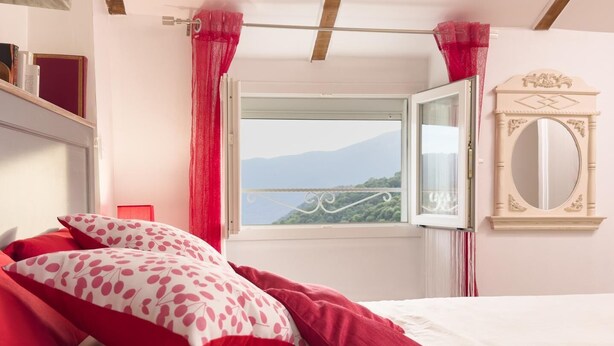 A bedroom with a bed, a window with a view, a mirror, and a shelf with books. - A MOLINA - ZICAVO - Gîte (ZICAVO)