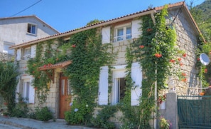 A stone house with a tiled roof, a wooden door, and windows with shutters. - A MOLINA - ZICAVO - Gîte (ZICAVO)