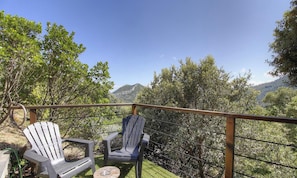 Ein Balkon mit zwei Adirondack-Stühlen, einem Holgitter und Blick auf eine gebirgige Landschaft.