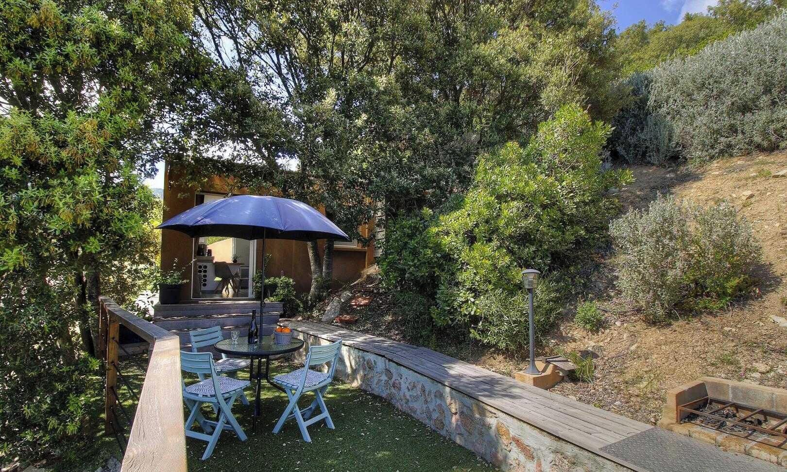 A patio with a table and chairs, a blue umbrella, and a stone wall.