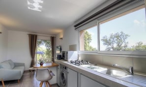 Eine kompakte Küche mit Waschmaschine, ein Essbereich mit Tisch und Stühlen sowie ein großes Fenster mit Blick auf Bäume.