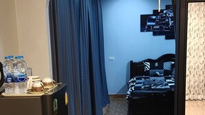 Habitación de hotel con kitchenette, cama con ropa de cama estampada, cortina azul y televisor montado en la pared.