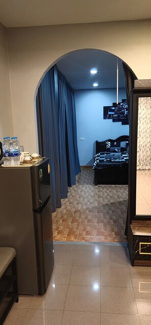 Ein Hotelzimmer mit einer Küchenzeile, einem Bett mit gemusterten Betttextilien, einem blauen Vorhang und einem am Wand montierten Fernseher.