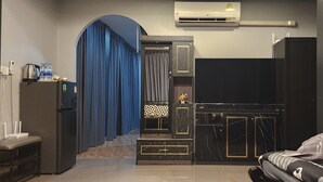 Una habitación de hotel pequeña con kitchenette, una cama, un escritorio y una cortina azul.