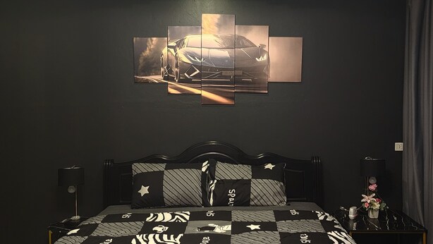 Un dormitorio con cama, una obra de arte en la pared, una mesita de noche, una lámpara y un altavoz.