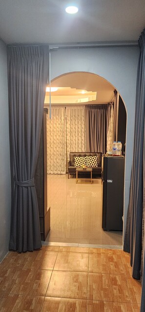 A room with a sofa, a small table, a refrigerator, and a patterned curtain. - Marin House Pattaya (Muang Pattaya)
