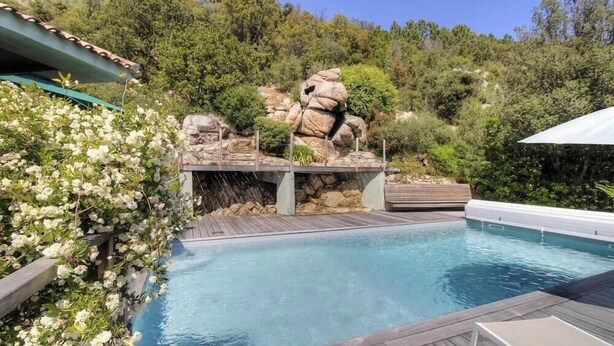 Ein Pool mit Holzterrasse, umgeben von üppiger Vegetation und einer Felsformation.