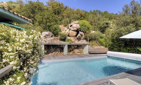 Ein Pool mit Holzterrasse, umgeben von üppiger Vegetation und einer Felsformation.