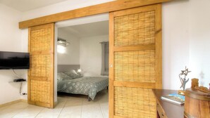 Ein Schlafzimmer mit Schiebetür, einem Bett, einem Nachttisch, einer Lampe, einem an der Wand montierten Fernseher und einem kleinen Regal.