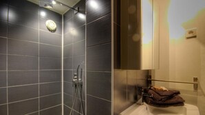 Un bany modern amb rajoles fosques, una dutxa, un lavabo i un mirall.