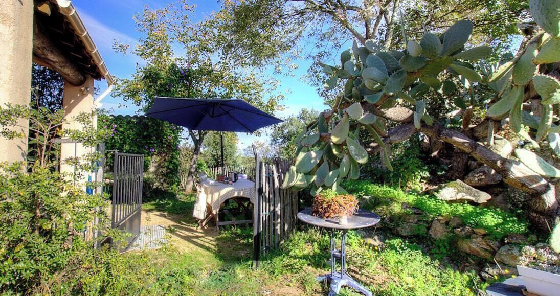 Un giardino con un tavolo e sedie, un ombrello blu e un cancello.