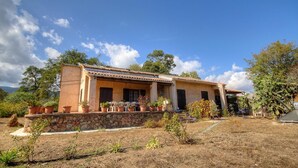 Una casa de dues plantes amb fonaments de pedra, teulada de rajoles i plantes en testos al jardí.