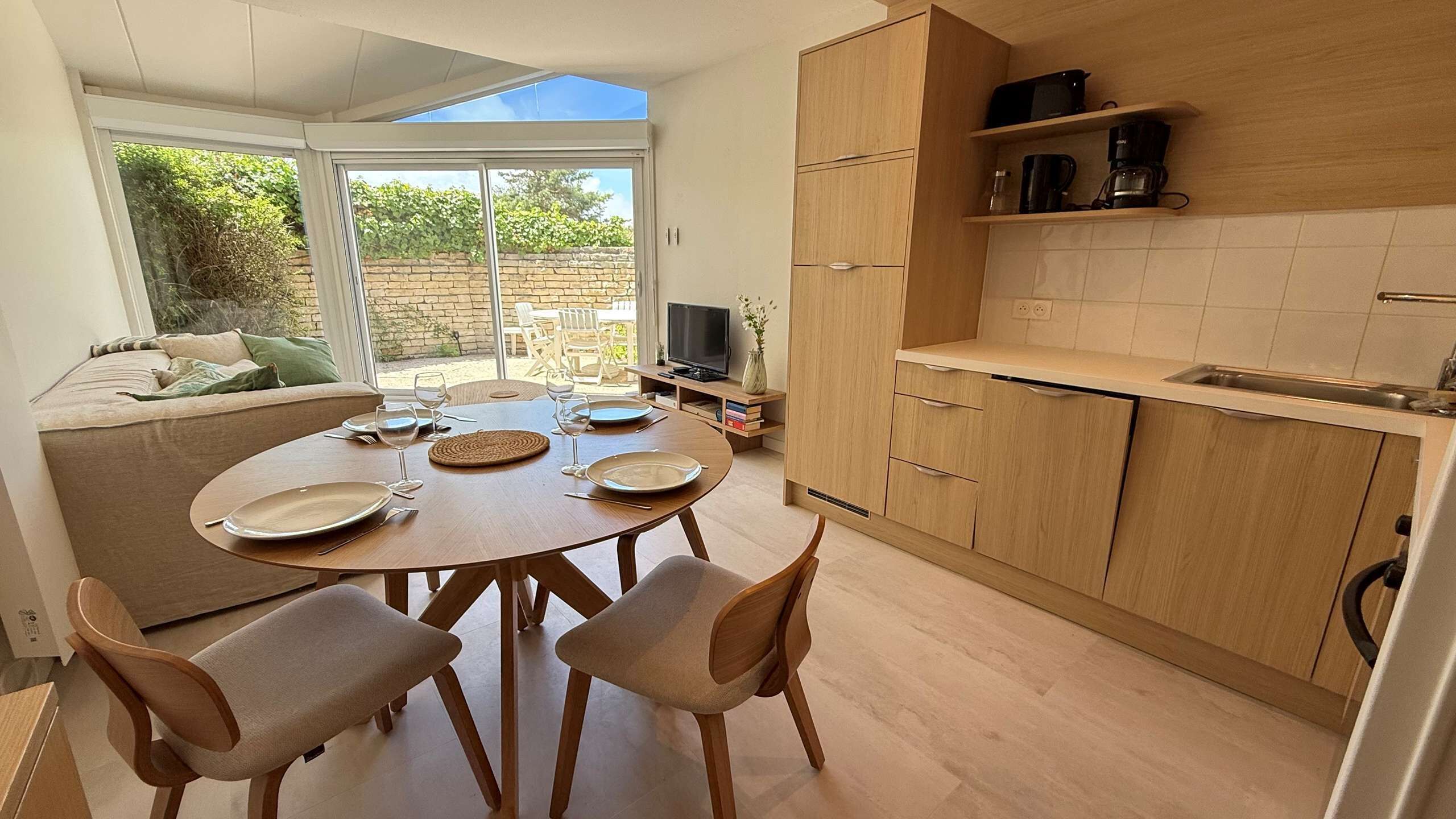 A dining area with a round table, four chairs, and a TV in the background.