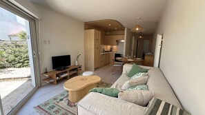 A modern living room with a sofa, TV, and dining area. - Renovated apartment with shared pool and parking (LA COUARDE SUR MER)