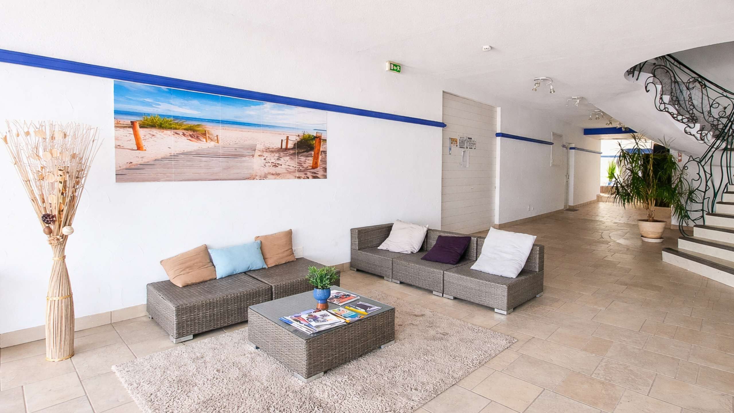 Un hall d’entrée agrémenté d’une grande fresque représentant une plage, de canapés en osier, d’une table basse et d ’un escalier.
