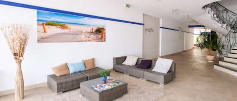 A lobby with a large beach mural, wicker sofas, a coffee table, and a staircase.