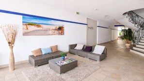 A lobby with a large beach mural, wicker sofas, a coffee table, and a staircase. - Renovated apartment with shared pool and parking (LA COUARDE SUR MER)