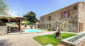 Ein Steinhaus mit Pool, Sitzgelegenheiten im Freien und einer Pergola.